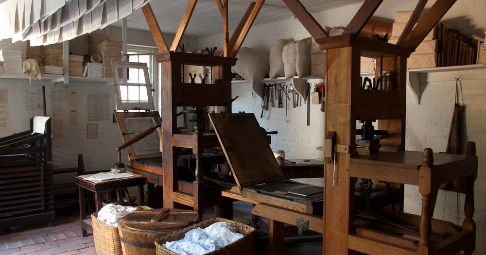 Eighteenth-century printing press with drying newspapers and rag supply.